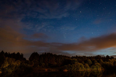 Evening landscape, a starry sky in the clouds and a comet over a forest lake. 