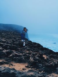 Woman photographing sea from cliff against sky