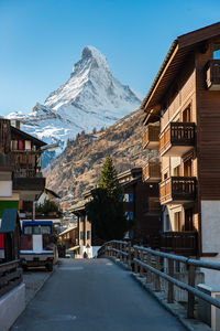 Snow covered road by buildings against clear sky