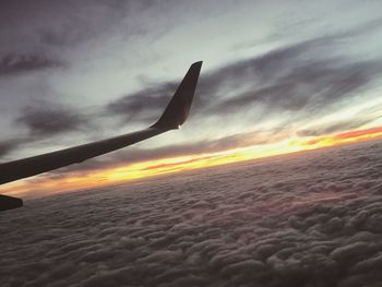 View of airplane wing over clouds during sunset