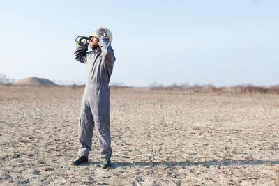 Man wearing protective workwear on field against clear sky