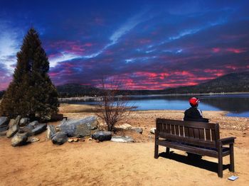 Rear view of child sitting on bench at beach against sky