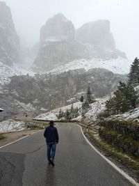 Rear view of man walking on mountain road during winter