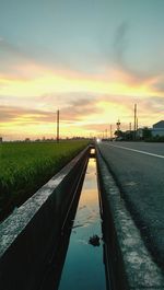 Gutter by field against cloudy sky during sunset