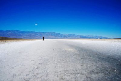 Man standing on sand dune in desert against blue sky