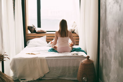 A young woman in pyjamas is sitting on a bed in a lotus position 