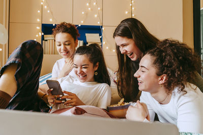 Happy young woman showing smart phone to female friends at home