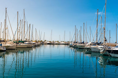 Sailboats moored in harbor against clear blue sky