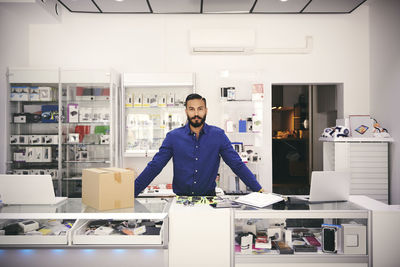 Portrait of confident owner standing at counter in electronics store