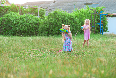 Two little girls play in the summer on a green meadow with water pistols