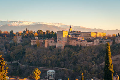 Breathtaking view of sunlit alhambra fortress complex located on lush hill near mountain range at sunrise in granada, spain