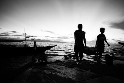 Silhouette men carrying crate at harbor during sunset