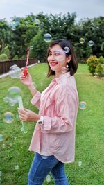 Smiling young woman with bubbles standing on field