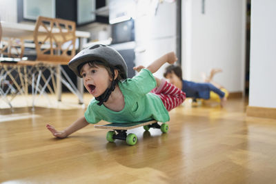 Toddler boy at home lying on skateboard wearing helmet having fun