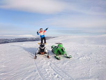 Full length of man standing by snowmobiles on snow against sky