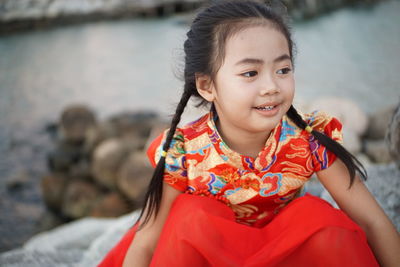 Smiling girl looking away while sitting on rocks against sea