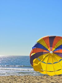 Multi colored parachute on beach against clear sky