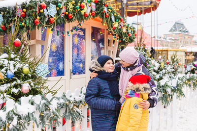 Smiling mother and kids standing against christmas decoration outdoors