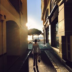 Rear view of man walking on street amidst buildings in city