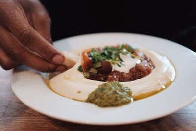 Cropped hand of person having food in plate at table