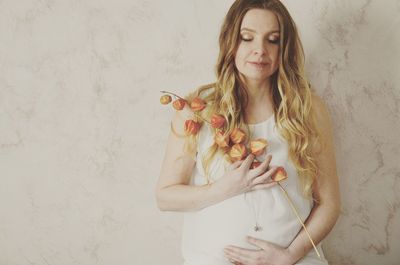 Pregnant woman holding winter cherries against wall