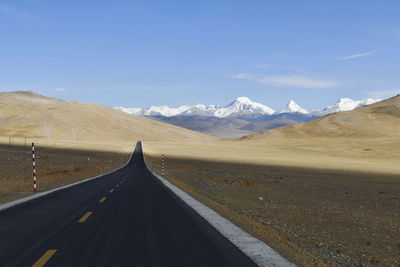 Empty road leading towards mountains against sky