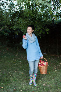 Happy beautiful woman holding apple with basket at orchard