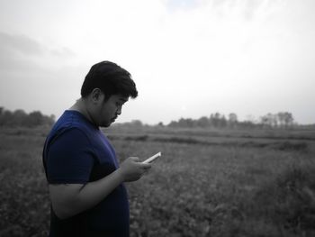 Side view of man using mobile phone while standing on field against clear sky