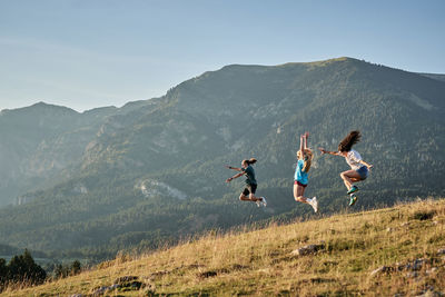 Company of delighted friends jumping on hill in mountains while enjoying freedom during summer vacation