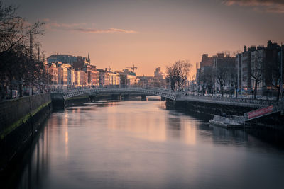 Bridge over river amidst buildings against sky during sunset