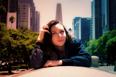 Portrait of beautiful young woman in city against sky