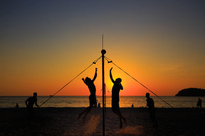 Silhouette people playing volleyball on beach against sky during sunset