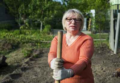 Portrait of mature woman with shovel standing at yard