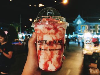 Close-up of hand holding drink in city at night