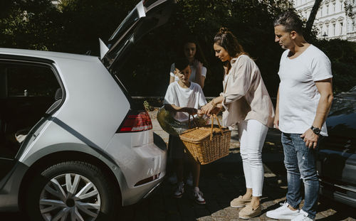 Family with picnic basket by electric car on road