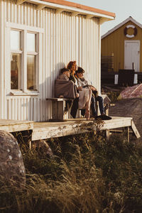 Mother sitting with sons against cabin during sunny day