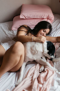 Smiling woman lying with dog on bed