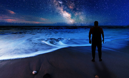 Rear view of man looking at sea during night