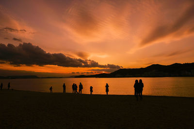 Silhouette people on beach against sky during sunset