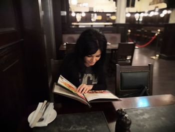 Woman reading book while sitting on table