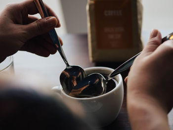 Cropped image of hands holding spoons in black coffee at cafe