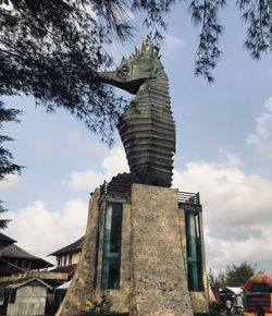 Low angle view of statue by building against sky