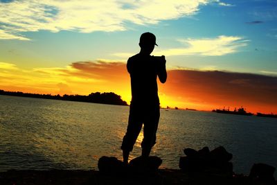 Silhouette man standing by sea against sky during sunset