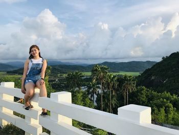 Young woman sitting on mountain against sky
