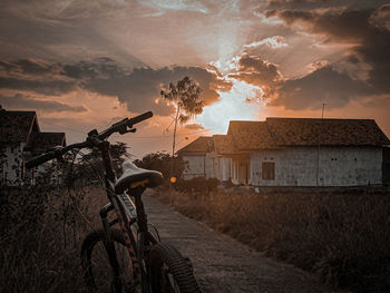 Bicycle on road amidst buildings against sky during sunset