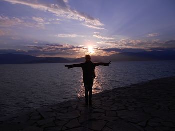 Silhouette person standing at beach against sky during sunset