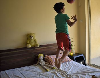 Full length of boy holding toy on bed at home