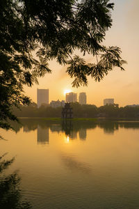 Scenic view of lake by buildings against sky during sunset