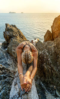 Midsection of man on rock at sea shore against sky