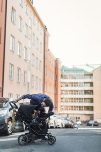 Mid adult man checking on baby in pushchair on city street